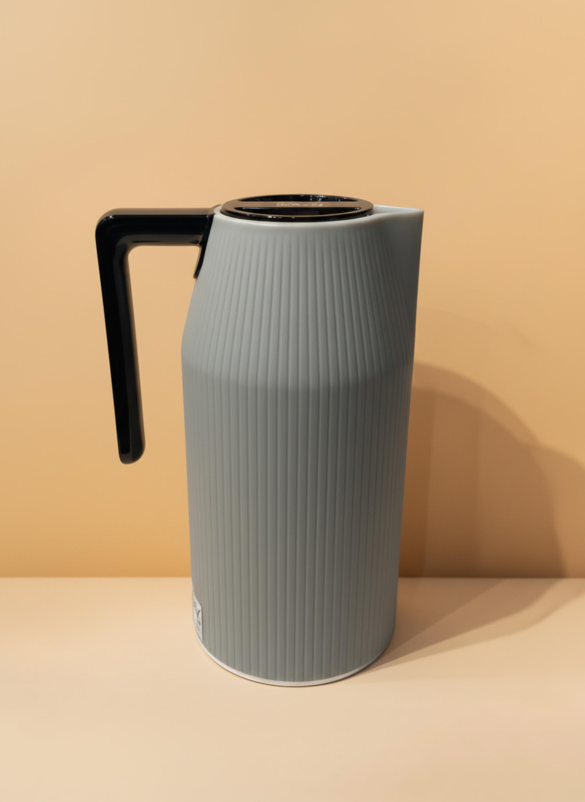 Gray pitcher with a black handle on a beige background